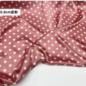 Peut inclure: Gros plan sur un tissu satin&eacute; rose avec un motif &agrave; pois. Le tissu est de couleur rose poudr&eacute; avec des pois blancs. Le texte "0,8 cm 皮粉" est dans le coin sup&eacute;rieur gauche. Le tissu est drap&eacute; et pli&eacute;.