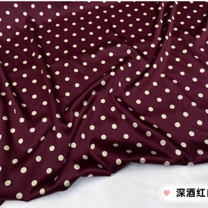 Peut inclure: Tissu bordeaux &agrave; pois blancs r&eacute;p&eacute;t&eacute;s. Le tissu est drap&eacute;, cr&eacute;ant des plis et des ombres. La texture g&eacute;n&eacute;rale semble lisse et peut-&ecirc;tre satin&eacute;e, avec un l&eacute;ger &eacute;clat.