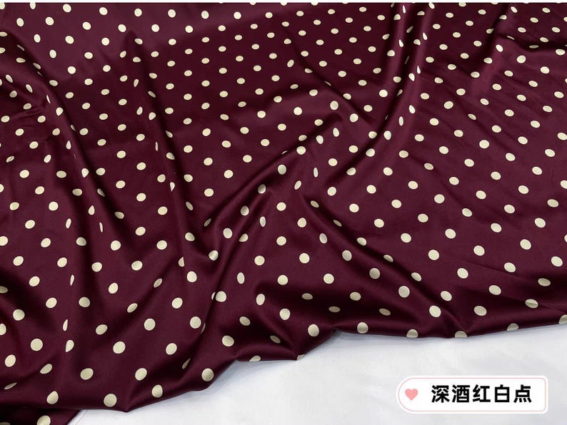 Peut inclure: Tissu bordeaux &agrave; pois blancs r&eacute;p&eacute;t&eacute;s. Le tissu est drap&eacute;, cr&eacute;ant des plis et des ombres. La texture g&eacute;n&eacute;rale semble lisse et peut-&ecirc;tre satin&eacute;e, avec un l&eacute;ger &eacute;clat.