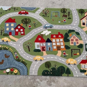 May include: A rectangular area rug featuring a colorful town scene with winding gray roads, green grassy areas, a blue pond with ducks, various houses with red roofs, trees, a playground with a swing set, and several small toy cars.