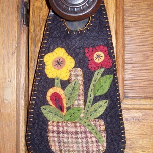 May include: A black felt door hanger with a brown and white plaid fabric basket and three felt flowers in yellow, red, and orange.
