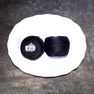 May include: Two spools of black embroidery floss, one with a DMC label that reads "310 N 8".