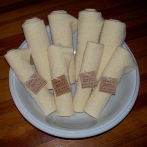 May include: A white bowl filled with eight rolls of pre-felted wool, each tied with a brown tag that reads "20% Wool Felt - Pre-Felted - Ready to Use - Fat 18 - 18 x 18" and a website address.
