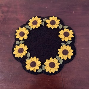 May include: A black felt round rug with a scalloped edge, decorated with yellow felt sunflowers. The sunflowers have brown centers and green leaves.