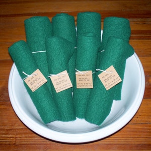 May include: A white bowl filled with seven rolls of green wool felt. Each roll is tied with twine and has a brown paper tag with the text "100% Wool Felt Pre-Felted Ready to Use Fat 1/8 - 6.75 x 12"  justfeltsandmore.com".