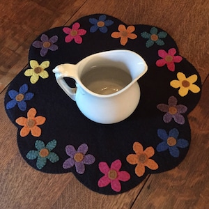 May include: A black felt table runner with a circle of colorful felt flowers around the edge. A white pitcher sits in the center of the runner.