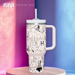 以下が含まれることがあります： 白いハンドルとストローが付いたトラベルマグ。ハリーポッターをテーマにした黒い線画のイラストが描かれています。マグには白い蓋とハンドルが付いています。「NAYA CREATIVE SOUL」の文字が左上にあります。