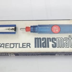 Könnte beinhalten: Ein technischer Stift Staedtler Marsmatic 700 in der Originalverpackung. Der Stift ist blau mit roter Spitze und silberner Kappe. Die Box ist weiß mit blauen Streifen und dem Text "marsmatic 700". Der Stift hat eine ISO-Kennzeichnung von 0,18 mm.