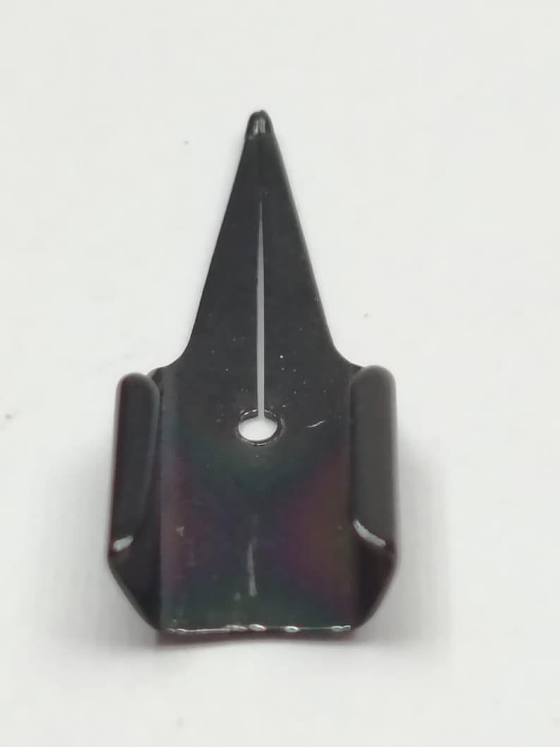 Puede incluir: Una plumilla de metal negro para pluma caligr&aacute;fica, con punta afilada y un peque&ntilde;o orificio circular. La plumilla tiene un acabado oscuro e iridiscente, dise&ntilde;ada para escritura y dibujo detallados.