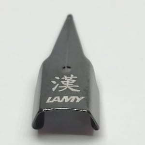 Puede incluir: Una plumilla negra con una punta afilada. La plumilla tiene la palabra "LAMY" y un car&aacute;cter chino grabado. La plumilla es de metal y tiene un acabado brillante.