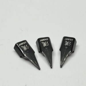 Puede incluir: Tres plumines negros de pluma estilogr&aacute;fica Lamy est&aacute;n colocados sobre una superficie blanca. Cada plum&iacute;n tiene el logotipo y el nombre de la marca Lamy. Los plumines est&aacute;n en &aacute;ngulo hacia la parte inferior derecha.