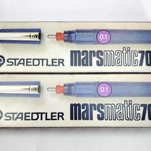 May include: Two STAEDTLER Marsmatic 700 technical pens in their original packaging. The pens are blue with a 0.1 mm tip, and the packaging is white with black and blue text. The pen caps are detached.