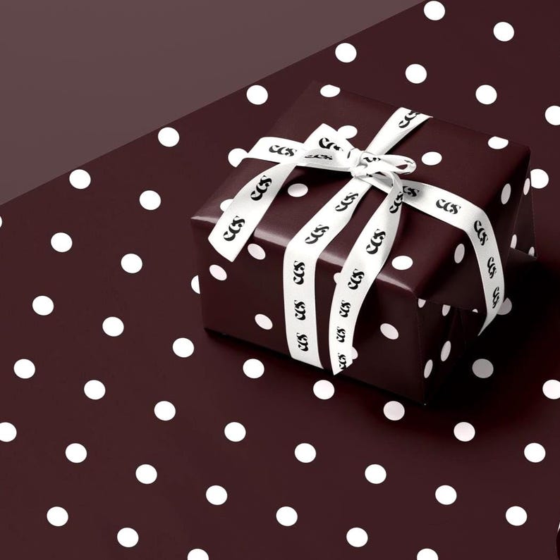 May include: A wrapped gift box with a dark burgundy polka dot pattern. The box is tied with a white ribbon featuring a repeating black logo. The gift is presented on a matching polka dot background.