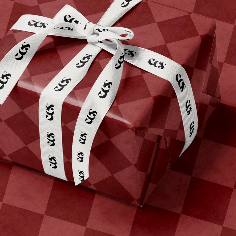 May include: A wrapped gift box with a red and white checkered pattern. The gift is adorned with a white ribbon featuring the repeating letters 'ccs' in black. The ribbon is tied into a bow on top of the box, with the ends of the ribbon cascading down the sides.