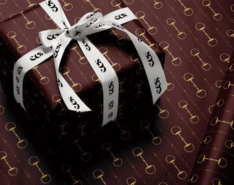 May include: A wrapped gift box with a white ribbon and bow. The gift wrap is a dark burgundy color with a repeating pattern of gold horse bits. The white ribbon has the letters "COS" printed on it.