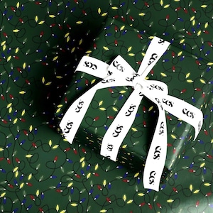 以下が含まれることがあります： 赤、青、黄色のクリスマスライトと黒い絡まったワイヤーの模様が繰り返されるダークグリーンの包装紙で包まれた長方形のギフトボックス。上部にはCCSという黒い文字が入った白いリボンが結ばれています。