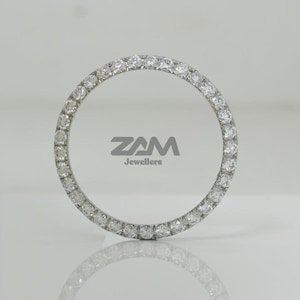 K&ouml;nnte beinhalten: Ein kreisf&ouml;rmiges Schmuckst&uuml;ck mit einem Ring aus kleinen, klaren Edelsteinen. Das St&uuml;ck ist vor einem wei&szlig;en Hintergrund platziert, mit dem Text "ZAM Jewellers" in Grau.