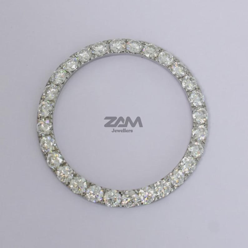 May include: Circular jewelry piece with numerous clear gemstones set in a silver-colored band. The gemstones are evenly spaced around the circle. The text "ZAM Jewellers" is visible in the center.