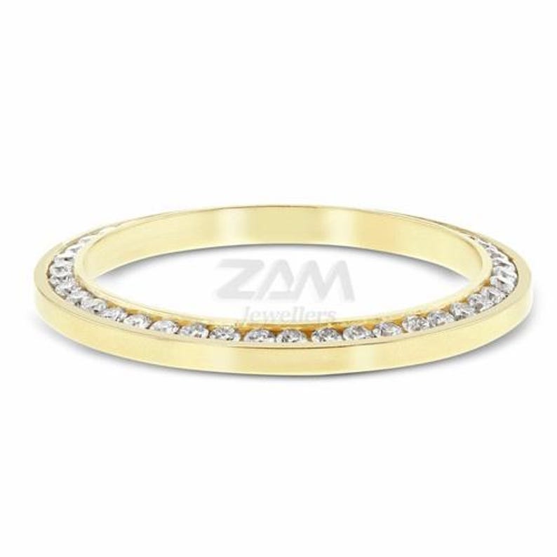 May include: A gold band ring with a row of small, clear gemstones set around the outer edge. The ring is a simple, elegant design, perfect for everyday wear. The ring is a size 7.