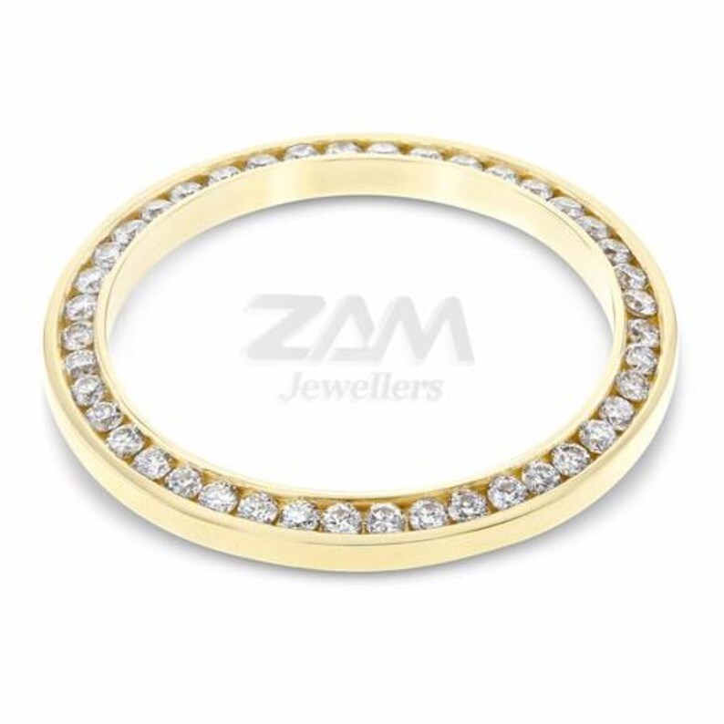 May include: A gold-colored ring with a circular design, featuring a row of small, clear gemstones set around the outer edge. The text "ZAM Jewellers" is visible in the center.