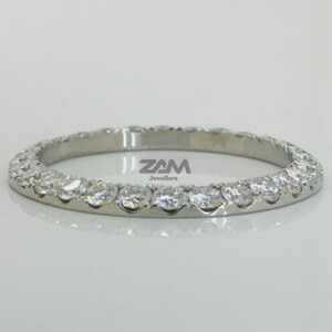 May include: A silver band ring with a continuous row of round-cut, clear gemstones. The ring is set against a white background, with the jeweler's logo visible. The ring appears to be approximately 0.25 inches in width.