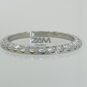 K&ouml;nnte beinhalten: Ein silberner Ring mit einer durchgehenden Reihe klarer, runder Edelsteine. Der Ring wird vor einem hellen Hintergrund pr&auml;sentiert. Der Text "ZAM Jewellers" ist auf dem Ring zu sehen.