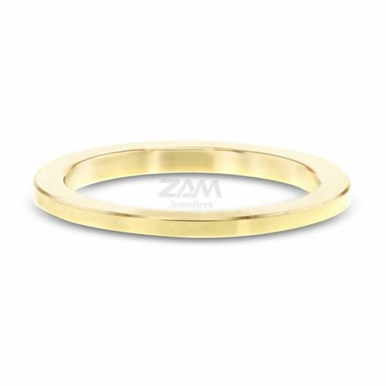 May include: A gold-colored ring with a flat, rounded design. The ring is made of a shiny, polished metal and is set against a white background. The text "ZAM Jewellers" is visible on the ring.