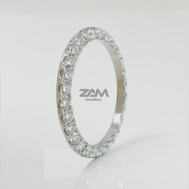 May include: A silver ring with a continuous row of round, clear gemstones. The ring is set against a white background, with the text "ZAM Jewellers" visible on the ring.