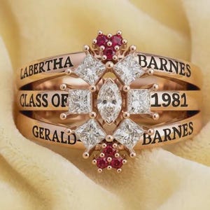 May include: Rose gold ring with the names LABERTHA BARNES and GERALD BARNES, and the text CLASS OF 1981. The ring features a central marquise-cut diamond, surrounded by square-cut diamonds and small red gemstones.