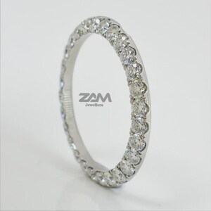 May include: A white gold eternity ring with a continuous row of round-cut diamonds. The ring is set with multiple small, sparkling diamonds. The ring is from ZAM Jewellers.