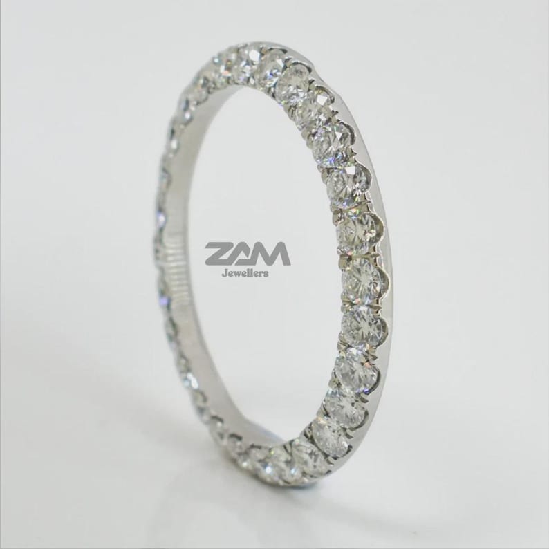 May include: A white gold eternity ring with a continuous row of round-cut diamonds. The ring is set with multiple small, sparkling diamonds. The ring is from ZAM Jewellers.