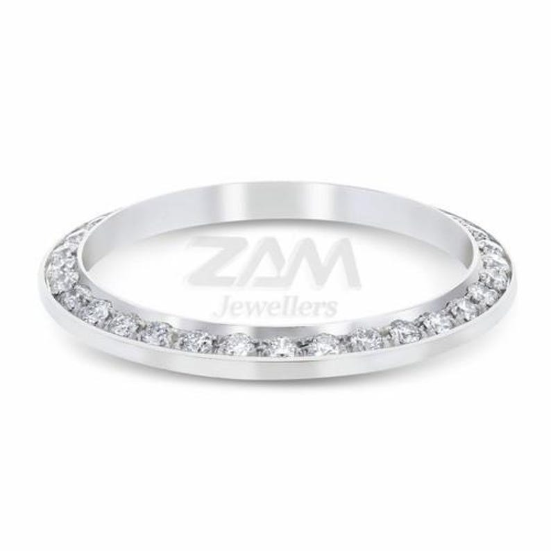 May include: A silver ring with a band of small, clear gemstones. The ring has a polished finish and the text "ZAM Jewellers" is visible in the center.