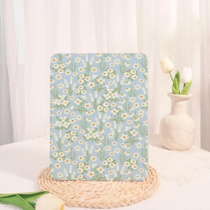 May include: A rectangular item with a light blue floral pattern. The design features white daisies and small white flowers with yellow centres, along with green stems and leaves. The pattern is set against a light blue background.