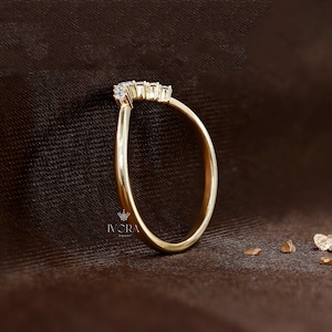 Puede incluir: Un anillo de oro con un dise&ntilde;o curvo, engastado con peque&ntilde;as piedras preciosas transparentes. El anillo se muestra sobre una superficie marr&oacute;n, con el logotipo de joyer&iacute;a IVORA visible. La banda del anillo es lisa y pulida.