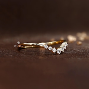 Puede incluir: Un anillo de oro curvado con una fila de peque&ntilde;as piedras preciosas redondas y claras. El anillo tiene un dise&ntilde;o delicado y elegante. El anillo est&aacute; sobre un fondo marr&oacute;n oscuro. La marca "IVORA" es visible.