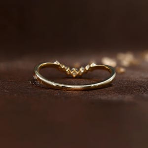Puede incluir: Un anillo dorado curvado con peque&ntilde;as piedras preciosas transparentes en la parte superior. El anillo tiene un acabado liso y pulido y est&aacute; sobre un fondo marr&oacute;n oscuro. La marca "IVCRA Jewelry" es visible.