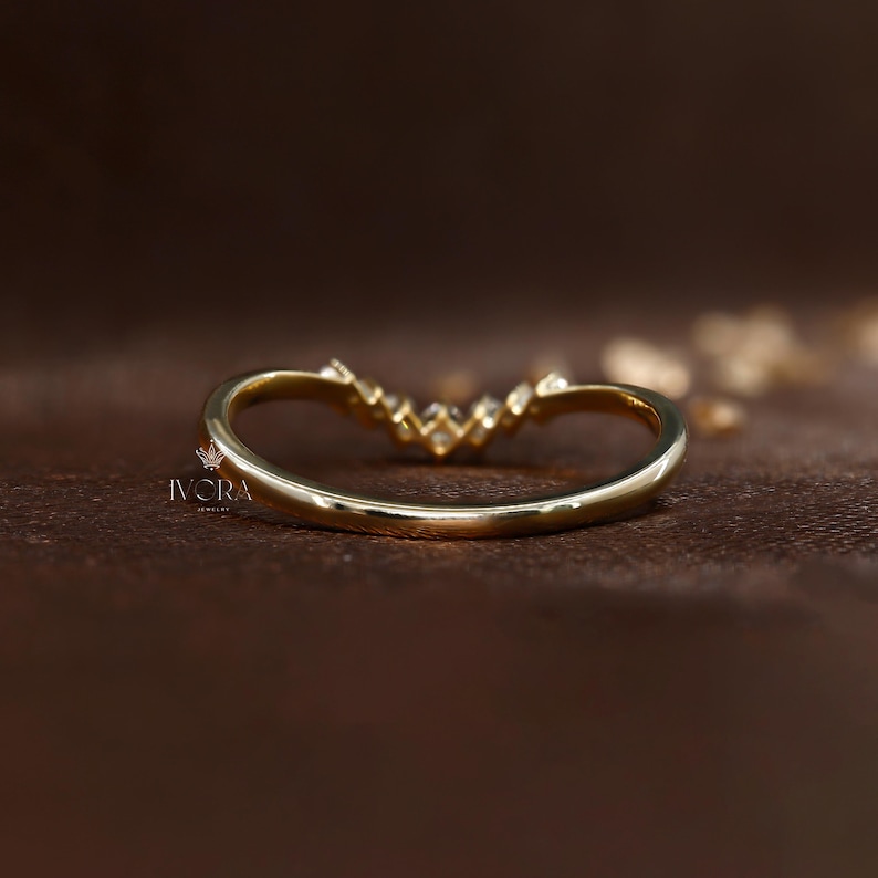 Puede incluir: Un anillo dorado curvado con peque&ntilde;as piedras preciosas transparentes en la parte superior. El anillo tiene un acabado liso y pulido y est&aacute; sobre un fondo marr&oacute;n oscuro. La marca "IVCRA Jewelry" es visible.