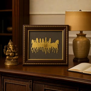 May include: A framed artwork featuring a gold-colored depiction of running horses. The artwork is set against a dark background within a brown wooden frame. A gold-colored statue of a deity and a lamp with a gold shade are also visible.