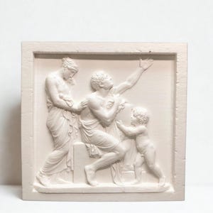 May include: A white relief sculpture depicting classical figures in a framed rectangular shape. The relief shows a man seated, reaching upwards, with a woman and a child nearby. The figures are draped in cloth.
