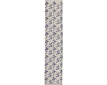May include: A rectangular table runner with a cream background and a repeating pattern of blue floral designs. The ends feature geometric patterns and fringe.
