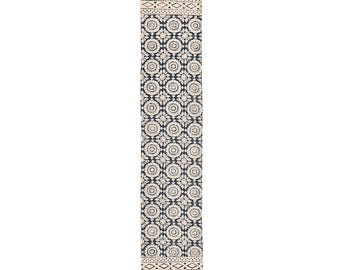 May include: A long, rectangular rug with a repeating floral pattern in cream and navy blue. The rug has a cream-colored border with geometric designs and fringe at both ends. The rug is designed for a hallway or entryway.