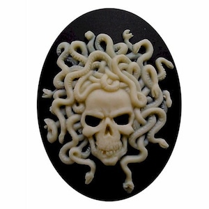 May include: Oval cameo featuring a skull with snake-like hair in a cream color, set against a black background. The skull has hollow eye sockets and a detailed jawline. The snakes are intricately sculpted.