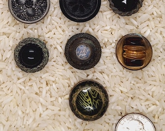 May include: Assortment of eight vintage buttons in various colours and designs, including black, brown, green, and red. The buttons are displayed on a white background.