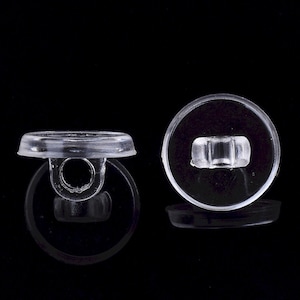 May include: Two clear plastic snap fasteners. Each fastener has a circular base and a top piece with a ring or a rectangular post. The fasteners are designed to connect two pieces of fabric or material together.