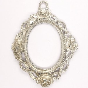May include: Silver-colored oval picture frame with floral and rope detailing. The frame features three rose designs and a loop at the top for hanging. The frame is empty, ready for a photo or artwork.