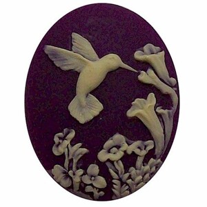 May include: An oval cameo featuring a hummingbird in flight, feeding from flowers. The hummingbird and flowers are a cream color, set against a dark purple background. The cameo is a classic, elegant design.