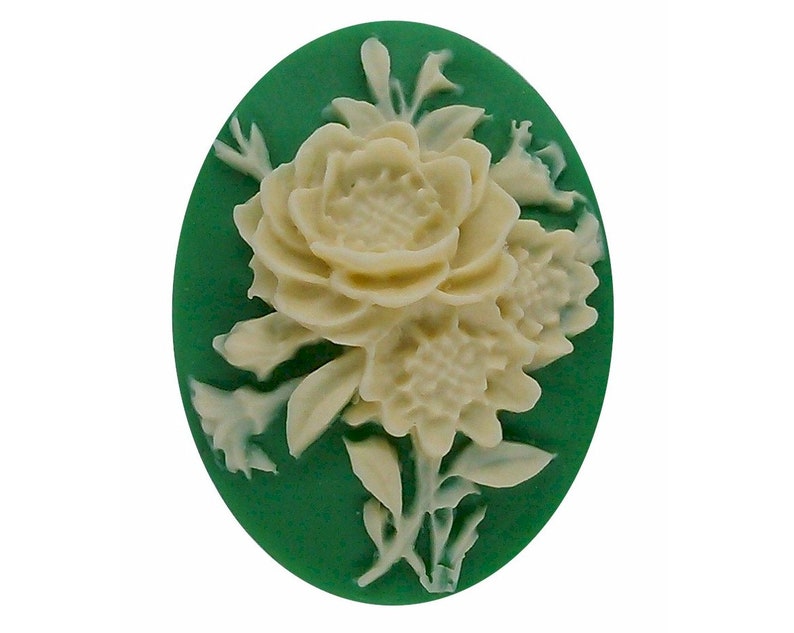 K&ouml;nnte beinhalten: Ovale Kamee mit cremefarbenem Blumendesign auf tiefgr&uuml;nem Hintergrund. Die Blumen sind aufwendig detailliert, mit mehreren Bl&uuml;tenbl&auml;ttern und Bl&auml;ttern. Ein klassisches Schmuckst&uuml;ck.