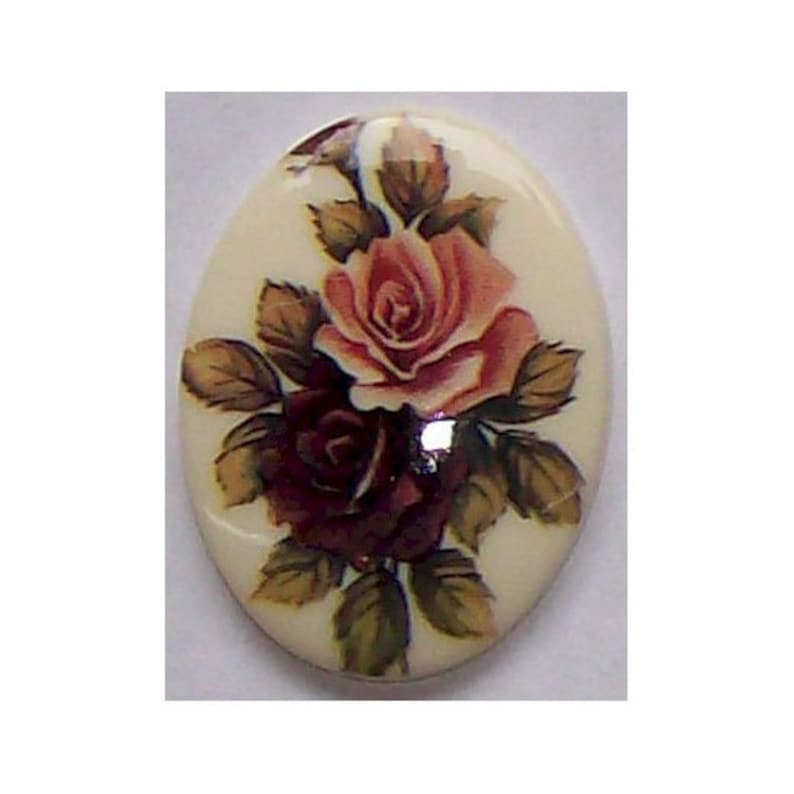 May include: Oval decorative item with a cream background. It features a detailed painting of two roses, one light pink and the other deep burgundy, surrounded by green and brown leaves. The item has a glossy finish.