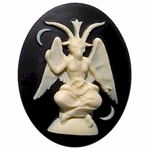 May include: A white cameo featuring a depiction of a goat-headed figure with wings, sitting on a pedestal against a black background. The figure has horns and a crown, and there are crescent moons on either side.