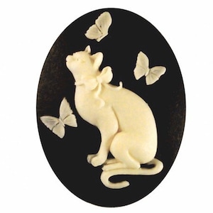 May include: A white ceramic cameo featuring a cat with a bow sitting on a black background with three white butterflies.